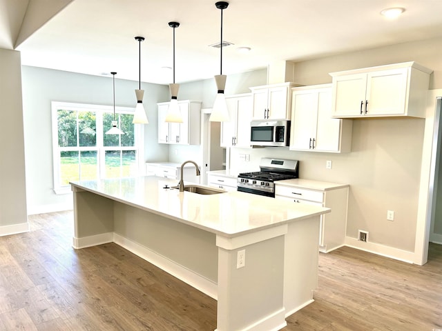 kitchen with white cabinets, a sink, a kitchen island with sink, light wood-style flooring, and stainless steel appliances
