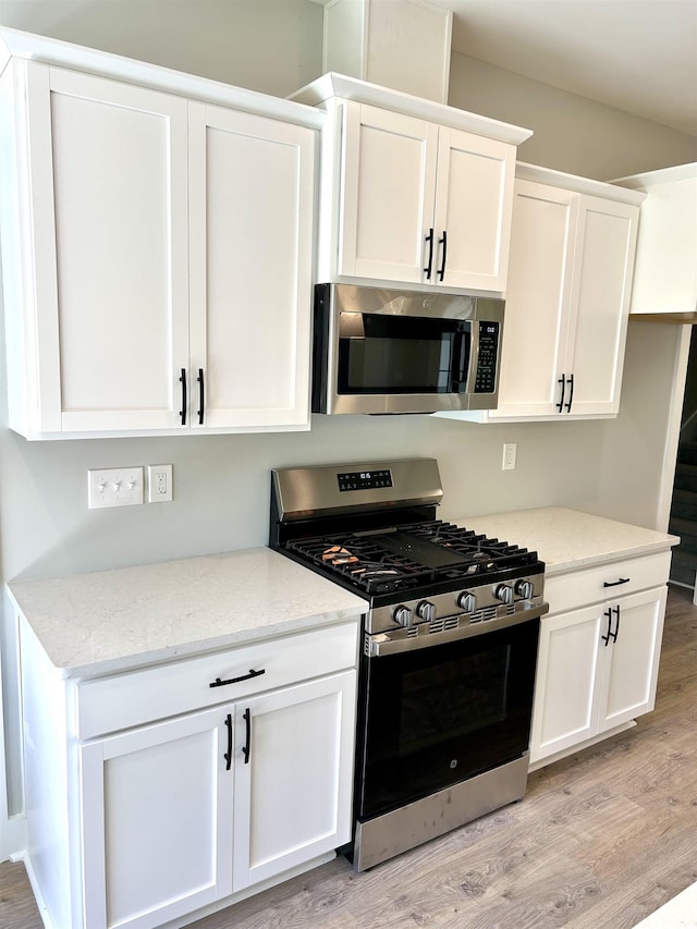 kitchen with light wood finished floors, appliances with stainless steel finishes, white cabinetry, and light stone countertops