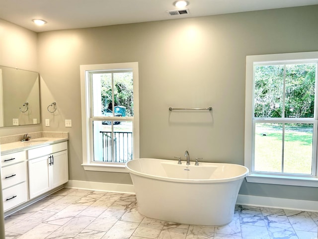 full bath featuring vanity, marble finish floor, baseboards, a freestanding tub, and a healthy amount of sunlight
