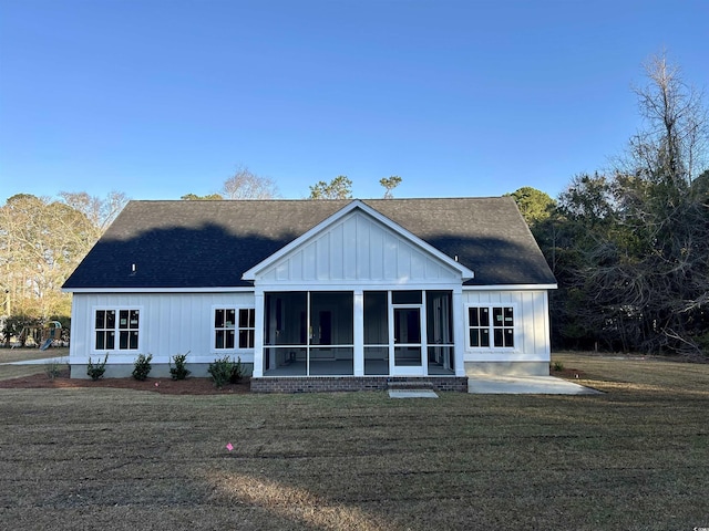 rear view of property with a shingled roof, a yard, board and batten siding, and a sunroom