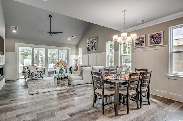 dining space with hardwood / wood-style floors, ceiling fan with notable chandelier, vaulted ceiling, and a healthy amount of sunlight