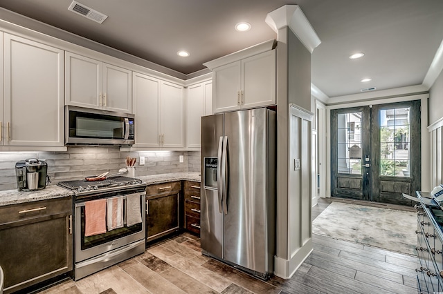 kitchen featuring backsplash, white cabinets, light hardwood / wood-style flooring, appliances with stainless steel finishes, and light stone counters