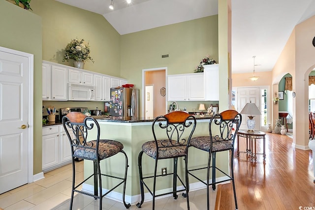 kitchen with white cabinetry, stainless steel appliances, kitchen peninsula, light hardwood / wood-style floors, and a breakfast bar area