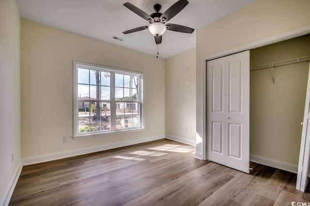 unfurnished bedroom with a ceiling fan, wood finished floors, visible vents, baseboards, and a closet