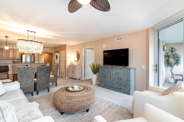 living room featuring light carpet, ceiling fan with notable chandelier, and stacked washing maching and dryer