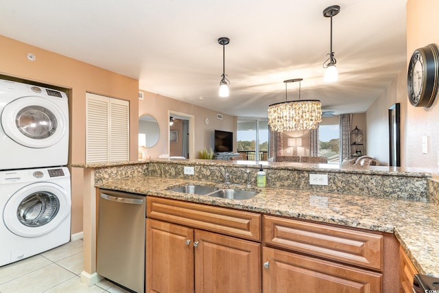 kitchen featuring dishwasher, sink, an inviting chandelier, stacked washer / dryer, and pendant lighting