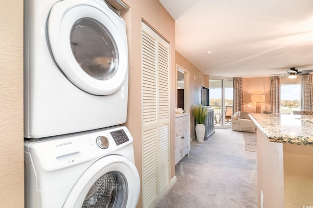 clothes washing area with ceiling fan, light colored carpet, and stacked washer / dryer