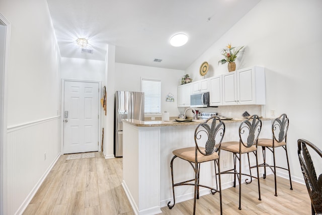 kitchen with kitchen peninsula, white cabinets, stainless steel appliances, and vaulted ceiling