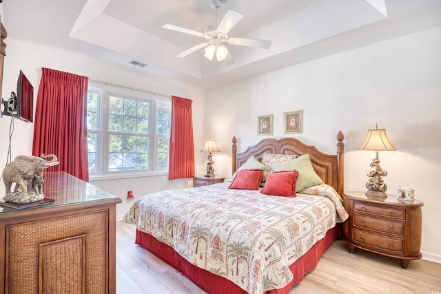 bedroom with a raised ceiling, ceiling fan, and light hardwood / wood-style floors