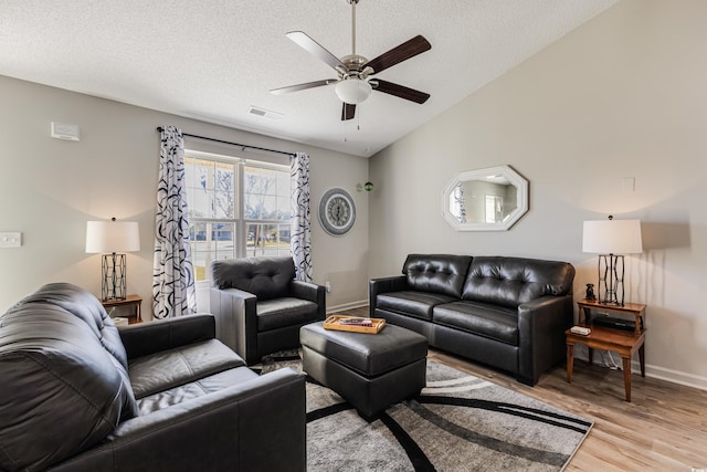 living room with a textured ceiling, ceiling fan, light hardwood / wood-style floors, and vaulted ceiling