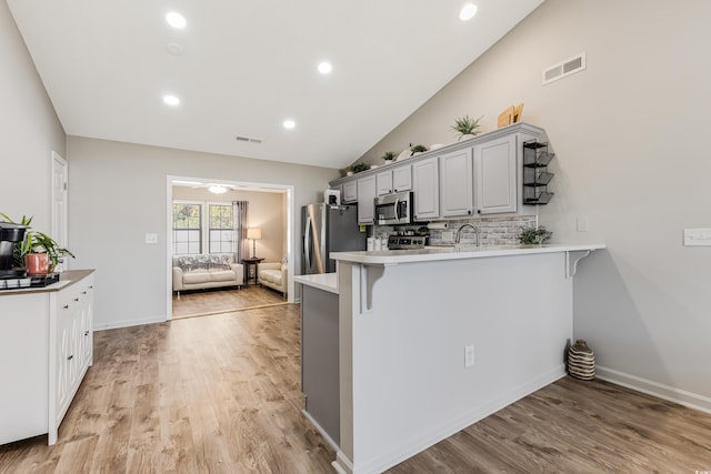 kitchen featuring a kitchen bar, appliances with stainless steel finishes, kitchen peninsula, and vaulted ceiling