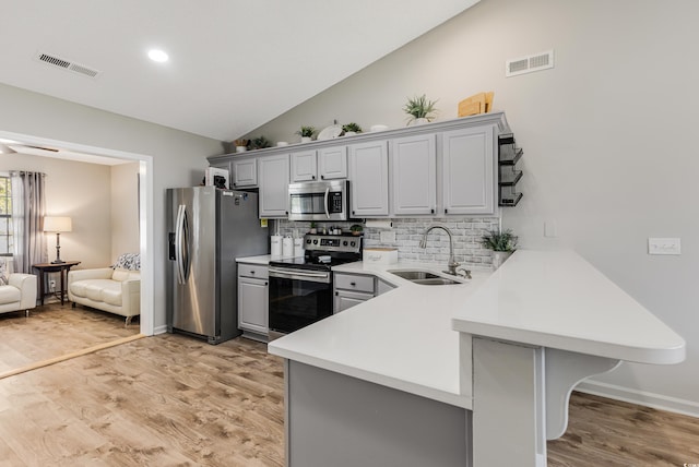 kitchen with kitchen peninsula, appliances with stainless steel finishes, a breakfast bar, sink, and gray cabinets