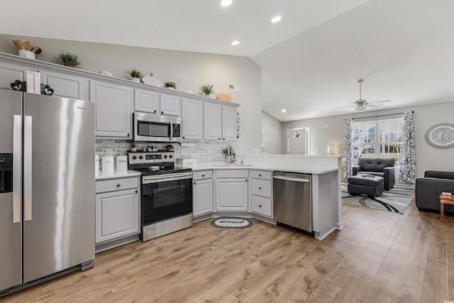 kitchen featuring lofted ceiling, sink, light hardwood / wood-style flooring, kitchen peninsula, and stainless steel appliances