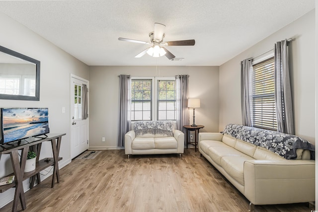 living room with ceiling fan, light wood-type flooring, and a textured ceiling