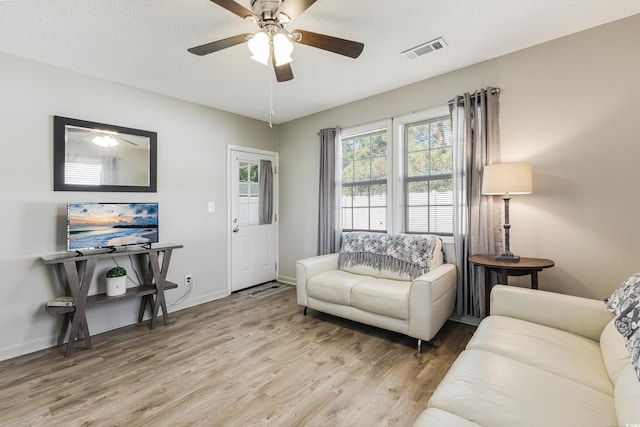 living room with ceiling fan, a textured ceiling, and light wood-type flooring