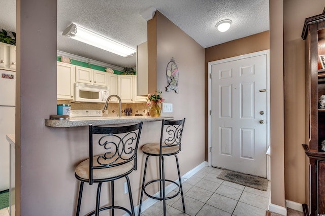 2226 Huntington Dr Unit D, Surfside Beach, SC 29575 - kitchen featuring white microwave, cream cabinetry, a textured ceiling, a breakfast bar, and baseboards