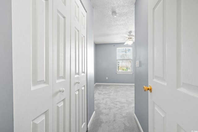 hall with baseboards, a textured ceiling, and light colored carpet