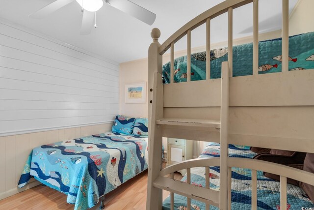 bedroom with hardwood / wood-style flooring, ceiling fan, and wooden walls