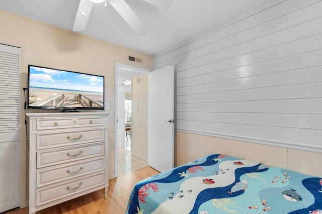 bedroom featuring light wood-type flooring, ceiling fan, and wooden walls