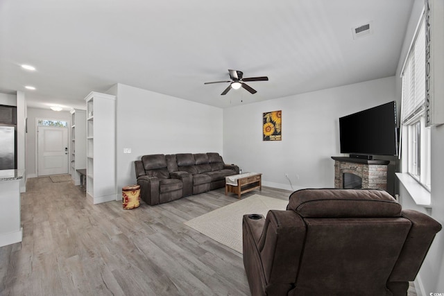 living room featuring a stone fireplace, a wealth of natural light, ceiling fan, and light wood-type flooring