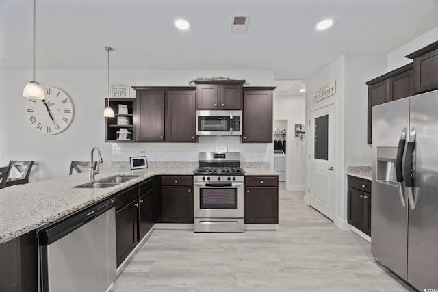 kitchen with sink, hanging light fixtures, light hardwood / wood-style flooring, dark brown cabinets, and appliances with stainless steel finishes