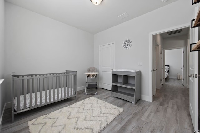 bedroom featuring light wood-type flooring and a nursery area