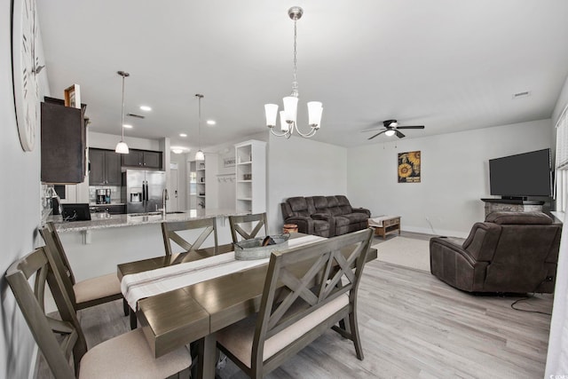 dining area featuring ceiling fan with notable chandelier, light hardwood / wood-style flooring, and sink