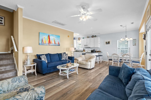 living room featuring ceiling fan with notable chandelier, wood-type flooring, crown molding, and a wealth of natural light