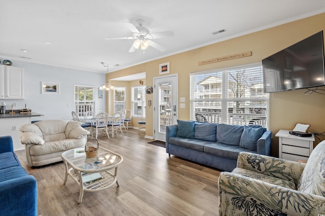 living room featuring crown molding, plenty of natural light, light hardwood / wood-style floors, and ceiling fan with notable chandelier