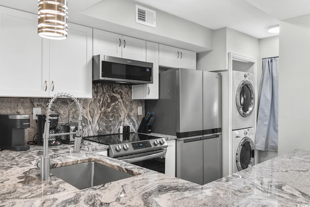 kitchen with backsplash, light stone countertops, stacked washing maching and dryer, white cabinetry, and stainless steel appliances