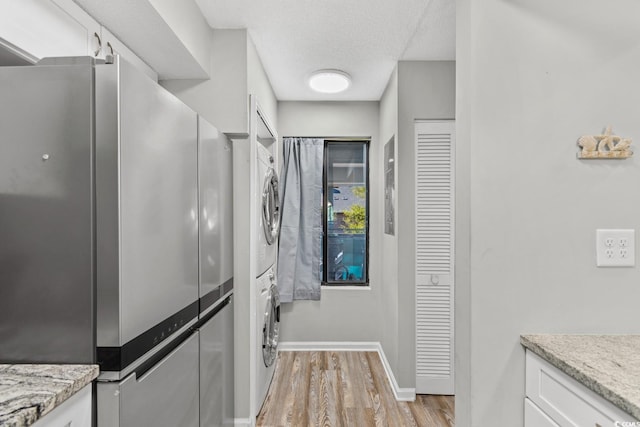 kitchen with light wood-type flooring, a textured ceiling, white cabinets, stainless steel refrigerator, and stacked washer / drying machine