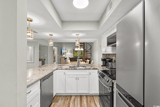 kitchen with kitchen peninsula, appliances with stainless steel finishes, sink, light hardwood / wood-style flooring, and white cabinets