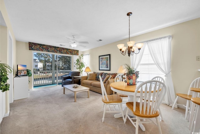 carpeted dining space with plenty of natural light and ceiling fan with notable chandelier