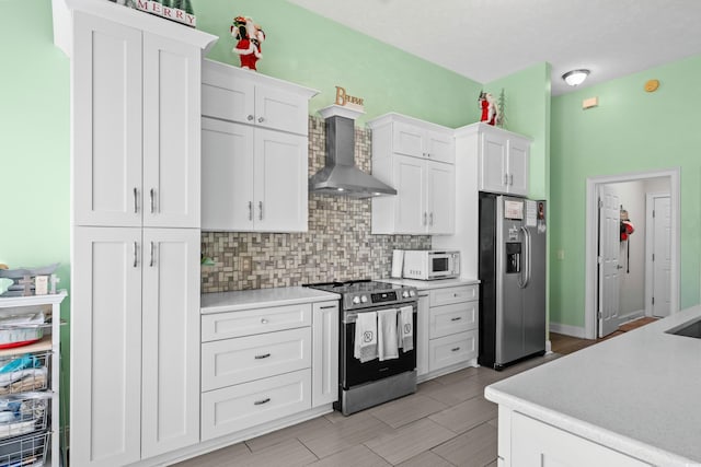 kitchen featuring tasteful backsplash, wall chimney range hood, light countertops, white cabinetry, and appliances with stainless steel finishes