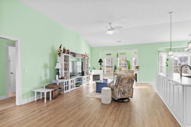 living area featuring light wood finished floors, vaulted ceiling, a ceiling fan, and a textured ceiling