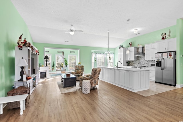 living room featuring ceiling fan, vaulted ceiling, light wood-style floors, and a textured ceiling