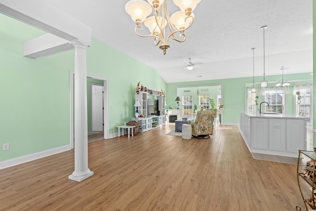 living area featuring light wood-type flooring, ornate columns, baseboards, and ceiling fan with notable chandelier