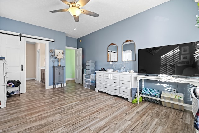 bedroom featuring ceiling fan, light wood-type flooring, a barn door, and baseboards