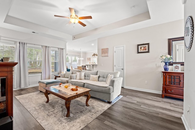 living room featuring dark wood-type flooring, ceiling fan, baseboards, and a raised ceiling