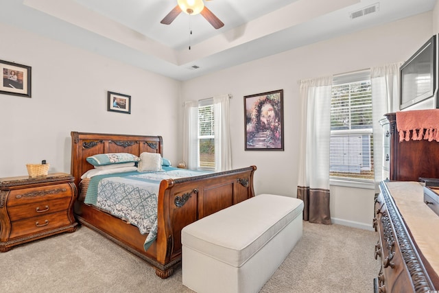 carpeted bedroom with a tray ceiling, multiple windows, and ceiling fan