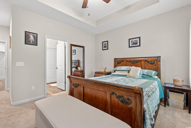 bedroom with light colored carpet, ceiling fan, a tray ceiling, and ensuite bathroom