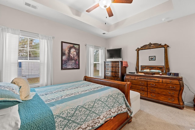 carpeted bedroom with a tray ceiling, ceiling fan, and visible vents