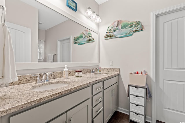 bathroom with wood finished floors, double vanity, a sink, and baseboards