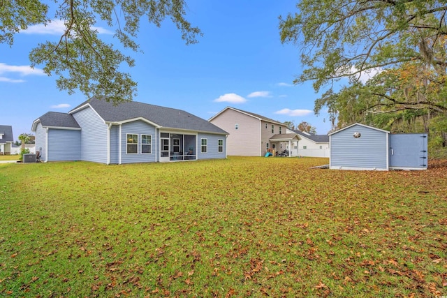 rear view of property featuring a sunroom, central AC unit, an outdoor structure, and a lawn