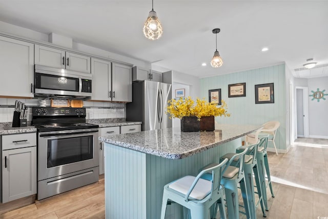 kitchen featuring light stone countertops, stainless steel appliances, light hardwood / wood-style flooring, a center island, and gray cabinets