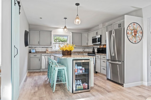 kitchen with beverage cooler, a barn door, light hardwood / wood-style flooring, a breakfast bar, and appliances with stainless steel finishes