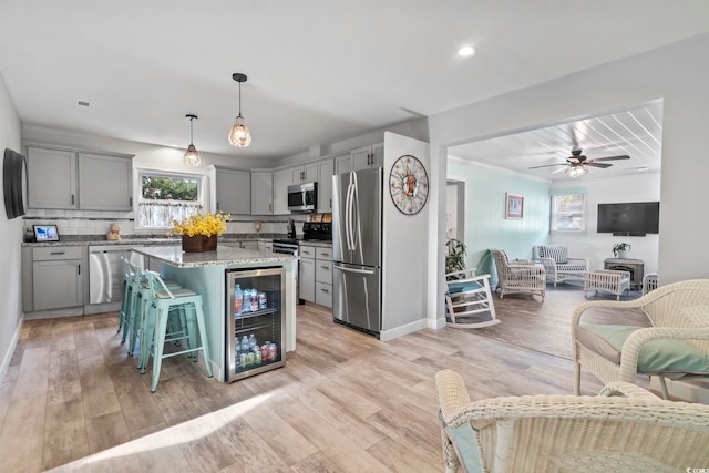 kitchen with appliances with stainless steel finishes, light wood-type flooring, pendant lighting, gray cabinets, and a kitchen island