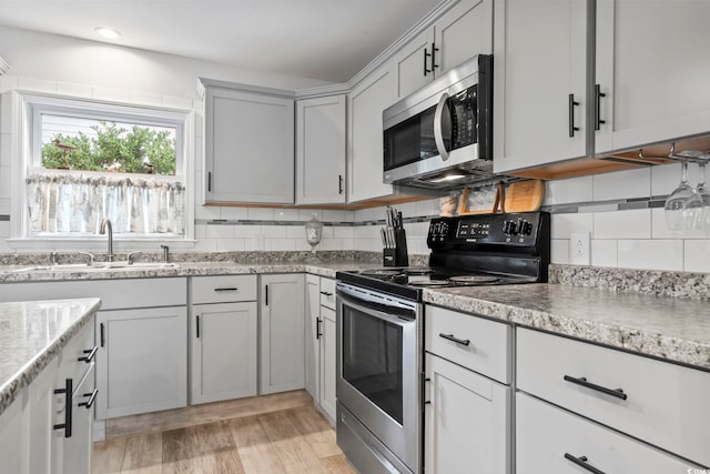 kitchen featuring backsplash, light stone counters, stainless steel appliances, sink, and light hardwood / wood-style flooring