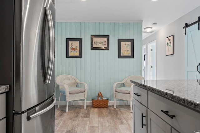 kitchen with stainless steel fridge, light stone counters, wooden walls, a barn door, and light hardwood / wood-style floors