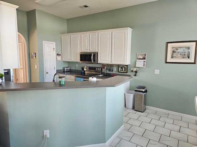 kitchen with kitchen peninsula, a textured ceiling, stainless steel appliances, and white cabinets